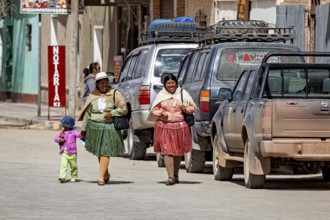 Two woman and a child in colorful, traditional clothing on a village street with an off-road