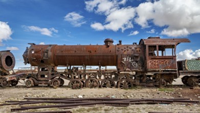 Rusted locomotive under a cloudy blue sky with graffiti along the body, old rusty locomotives at