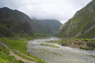 Wide valley with a river surrounded by imposing green mountains with clouds, Tergi River, Terek,
