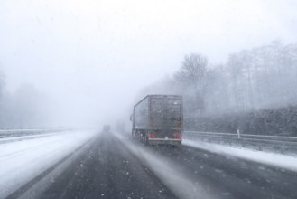View through the windshield of a passenger car driving through light snowblowing on partly