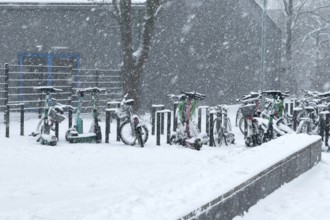 Tailored parked e-scooters and bicycles in winter during snowfall with snowflakes in the picture,