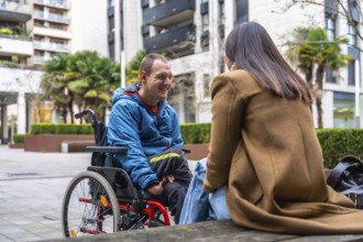 Young man in a wheelchair smiling and talking with a woman outdoors in an urban setting,