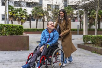 Caregiver pushing a man in a wheelchair on a paved path in an urban park, sharing a happy moment