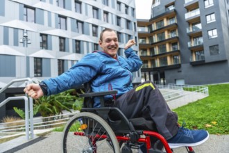 Man in wheelchair smiling and raising fists in victory on a city sidewalk by a modern building and