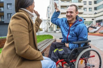 Joyful disabled man in a red wheelchair sharing a high five with a woman on a bench, symbolizing