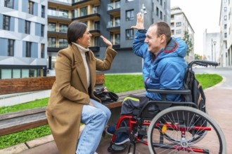 Young man with a physical disability sitting in a wheelchair and celebrating with a high five,