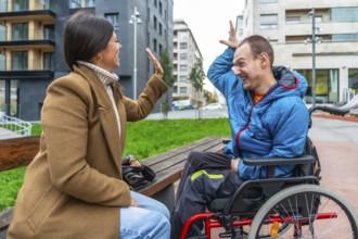 Young woman on a bench in the city happily high fiving a smiling man in a wheelchair, illustrating