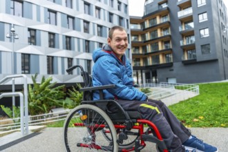 Happy man with a disability using a wheelchair on an accessible ramp in front of modern buildings,