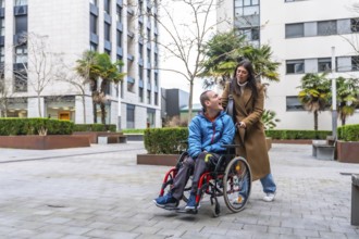 Woman pushing smiling man in a wheelchair along a city sidewalk, conveying everyday support,