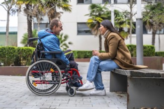 Man with a disability in a wheelchair having a cheerful conversation with a woman sitting on a park