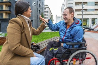 Young man with a disability sitting in a wheelchair and joyfully high fiving a woman sitting on a