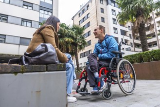 Young man with disability in a wheelchair discussing and smiling with a caring woman sitting on a