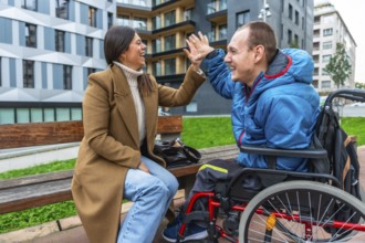 Woman and disabled man in wheelchair laughing, high fiving, and sharing a happy moment during an