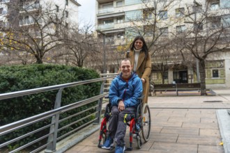 Happy woman caregiver assisting a young man with a disability, pushing him in his wheelchair along