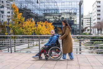 Woman pushing a smiling man in a wheelchair along an urban sidewalk during autumn, showcasing