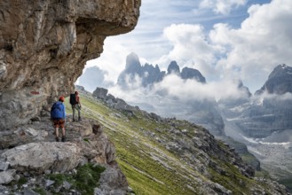Two mountaineers on a path in front of a picturesque mountain landscape with rocky peaks, Via