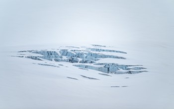 Smooth white snowy area on the glacier broken by crevasses with blue rugged glacial ice, detail,