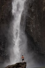 Daytime scene at Wallaman Falls with a fit man in swim trunks below the waterfall, Queensland,