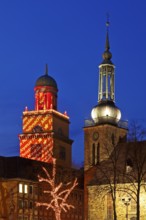 The Christmassy illuminated town hall tower and the illuminated church tower of St. John's Church