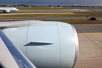Aircraft turbine near the runway with a passing car and another aircraft in the background, view