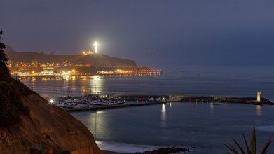 Coastal landscape at night with illuminated cross on a hill and harbor lights, calm sea atmosphere,