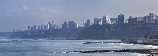 View of a coastal town with skyscrapers on cliffs and waves under a blue sky, The coast with the