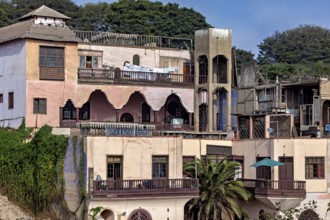 Historic buildings with decorated facades and balconies, surrounded by trees. Colourful and lively