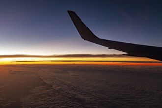 Airplane wings in front of a sunset over clouds, In an airplane above the clouds