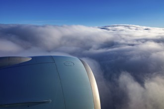 View from an airplane window of an engine and underlying clouds in the blue sky, on the plane above