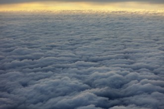 Dense, wavy cloud cover in grey sky, above the clouds on an airplane
