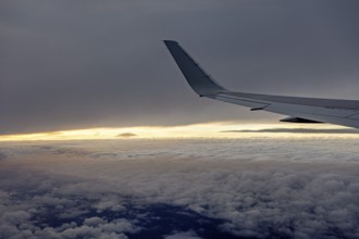 View of airplane wings at sunset over clouds, In an airplane above the clouds