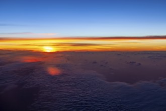 Bright colors of a sunrise over a cloud cover in the sky, on an airplane above the clouds