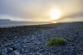 A peaceful beach at sunset with rocks and calm sea under a slightly cloudy sky, Båtsfjord,