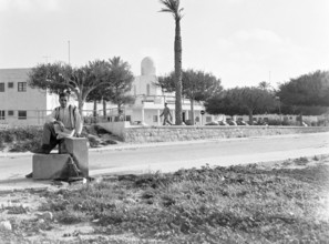 Young man sitting on low wall on street, Tripoli, Libya, North Africa 1956