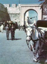 Horse drawn taxi in foreground, people walking in street, Bab al-Khendig archway city gate,