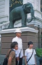Tourists pose for photo in front of palace guard, Grand Palace at Wat Phra Kaeo, Bangkok, Thailand,