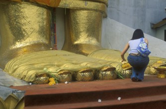 A young woman places flowers on the toes of the standing Buddha at Wat Indrawihan, Bangkok,