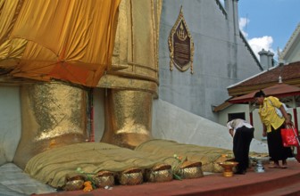 Women place flowers on standing Buddha's toes at Wat Indrawihan, Bangkok, Thailand, December 2002,