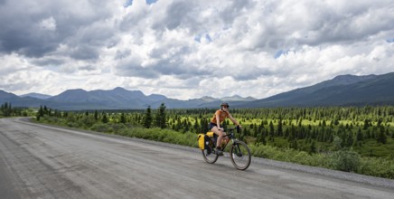 Young woman riding a bicycle on a dirt road through the tundra, mountainous landscape, Denali Park