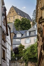Enge Gasse in Marburg with historic half-timbered and stone buildings under a wooded hill, The