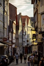 A picturesque old town street with half-timbered houses and walkers in an evening atmosphere, The