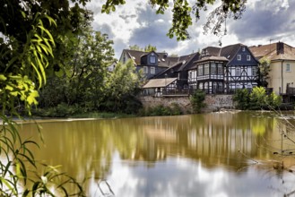 Half-timbered houses are reflected in the water in partly cloudy skies. The historic houses of