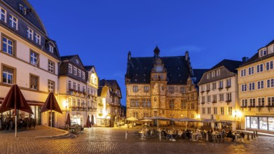 Historic square at dusk, surrounded by half-timbered houses and cobblestones, illuminated by warm