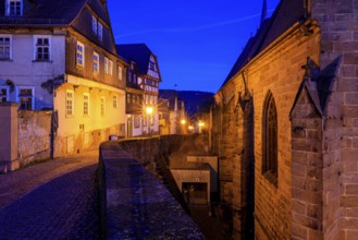 Historic street view at dusk with illuminated half-timbered houses and a church building, At the