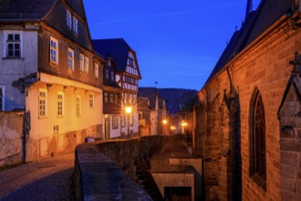 A nocturnal old town with half-timbered houses and cobblestones, warm lantern light creates a