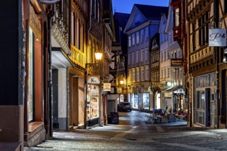 Narrow old town alleyway at night with illuminated shops and historic half-timbered buildings, At