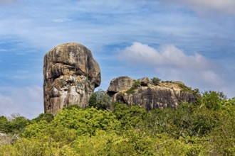 An impressive rock formation rises high above a green forest under a partly cloudy sky, the