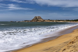 A peaceful coastal scene with sandy beach, turquoise ocean and distant rocks under blue skies, the