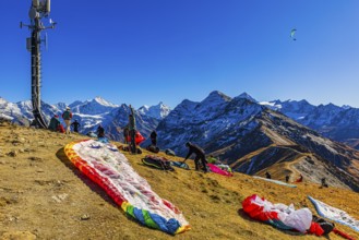 Paragliders are preparing for their start, with the snow-capped peaks of the Valais Alps, Val
