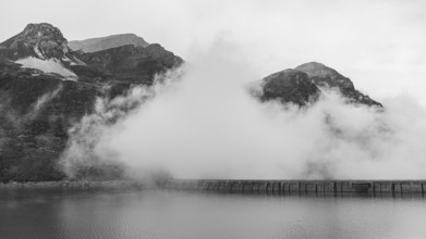 Fog rises over the dam of the Lac de Moiry reservoir, black and white photo, Val d'Anniviers,